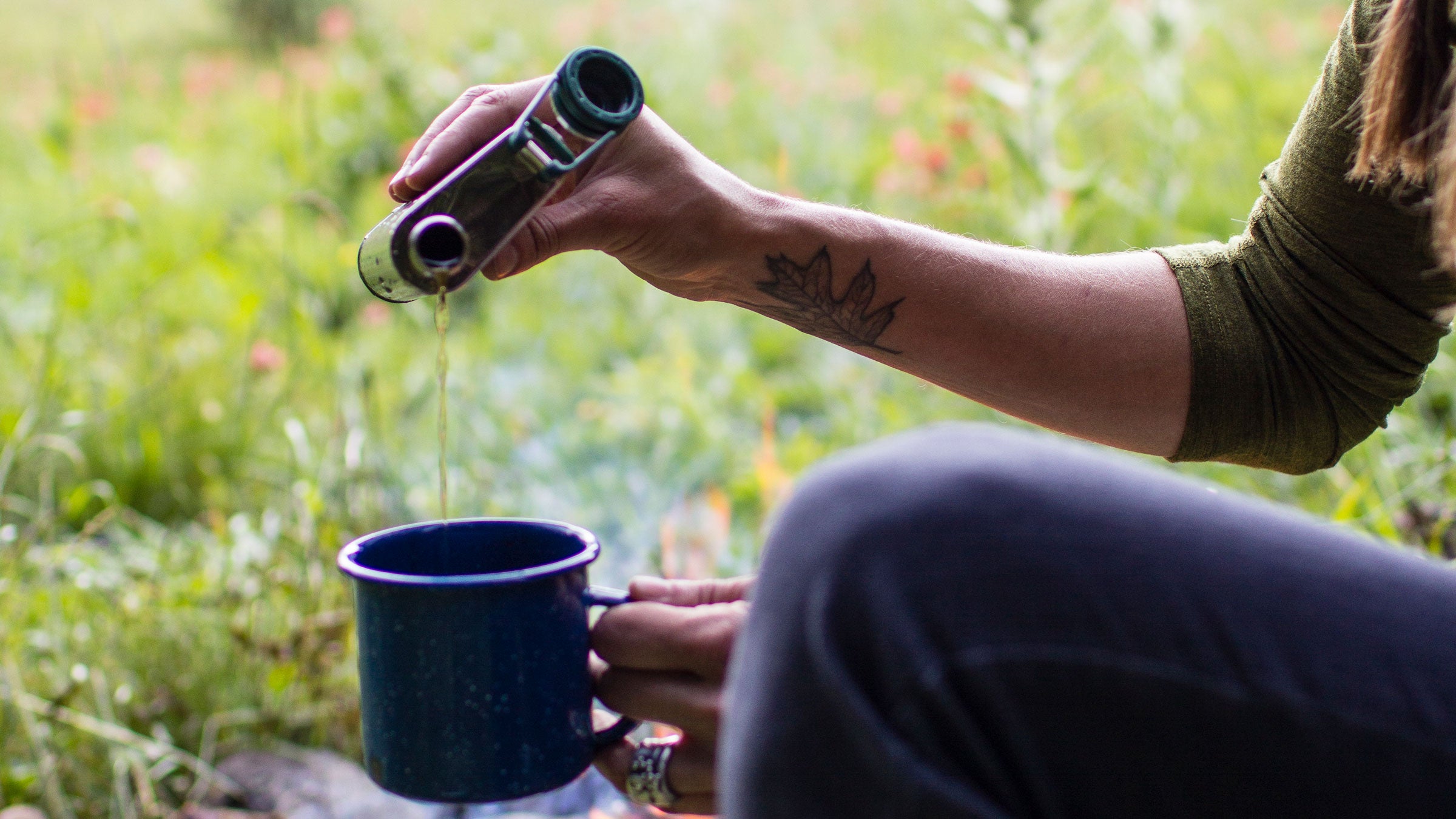 woman in field pouring flask into mug