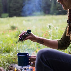 woman in field pouring flask into mug