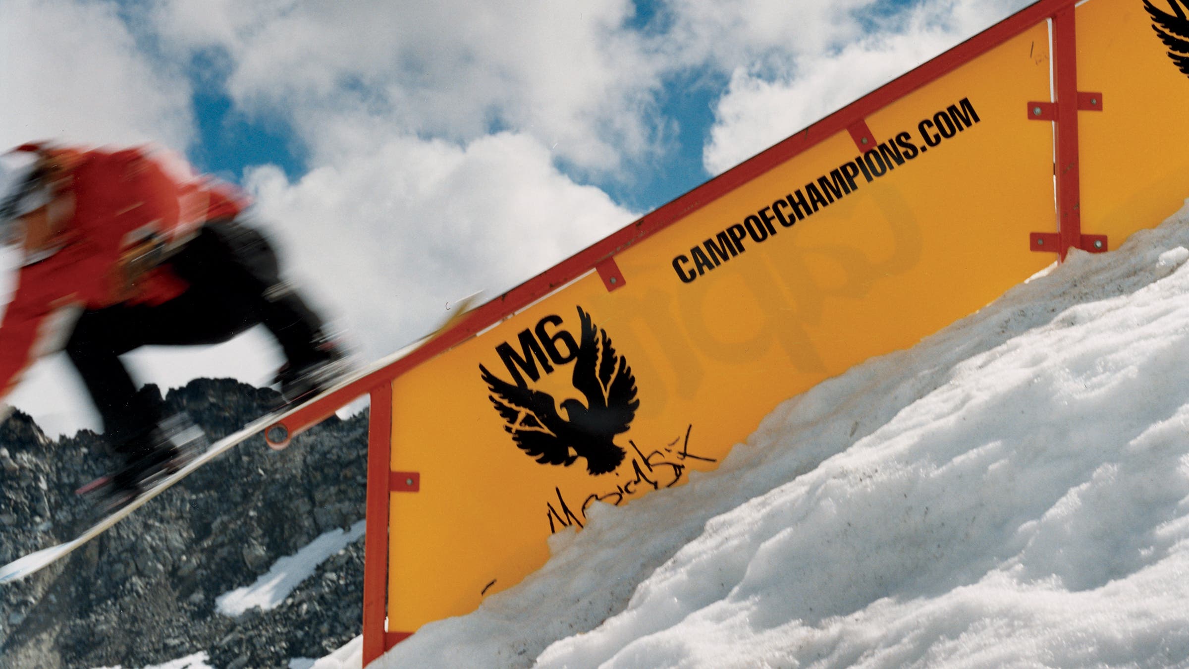 snowboarder in red jacket riding a rail over a yellow sign