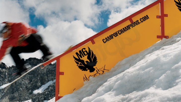 snowboarder in red jacket riding a rail over a yellow sign