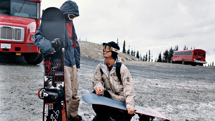 Two snowboarders with their boards in the parking lot