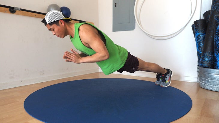 man clapping hands below him in plank position, with top half hovering over the ground and feet still on gym floor