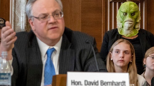 A protester stands behind Bernhardt at the acting Interior Secretary's Senate confirmation hearing.