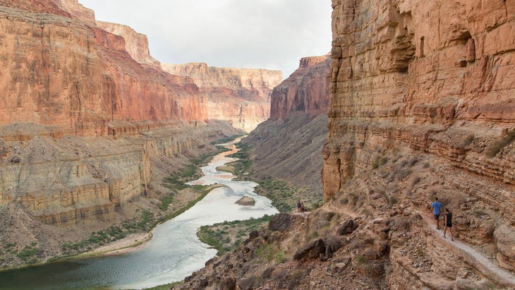 two hikers on singletrack against a red cliff over the Colorado River