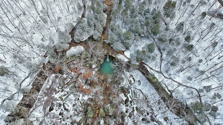 aerial shot of snowy trees and green waterfall