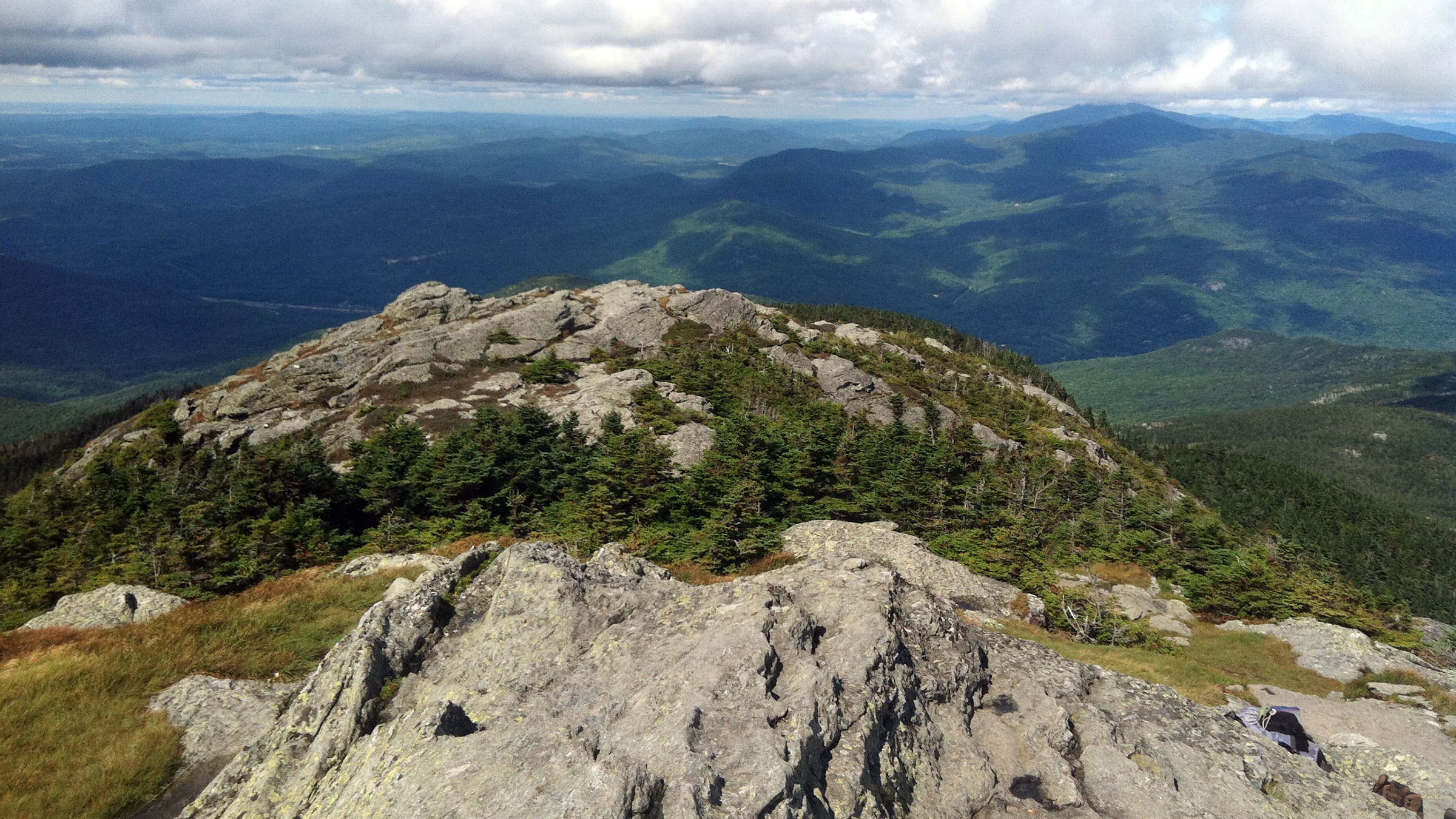gray cliff overlooking very high vista of forest and hills, blue and green