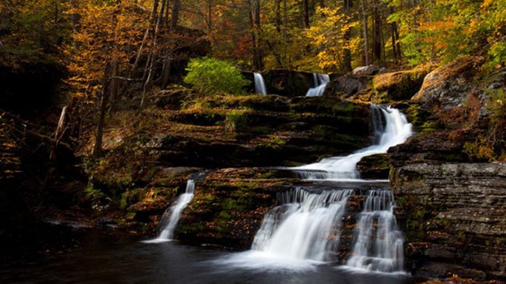 waterfall racing down brown rocks with yellow leaves on trees in the back