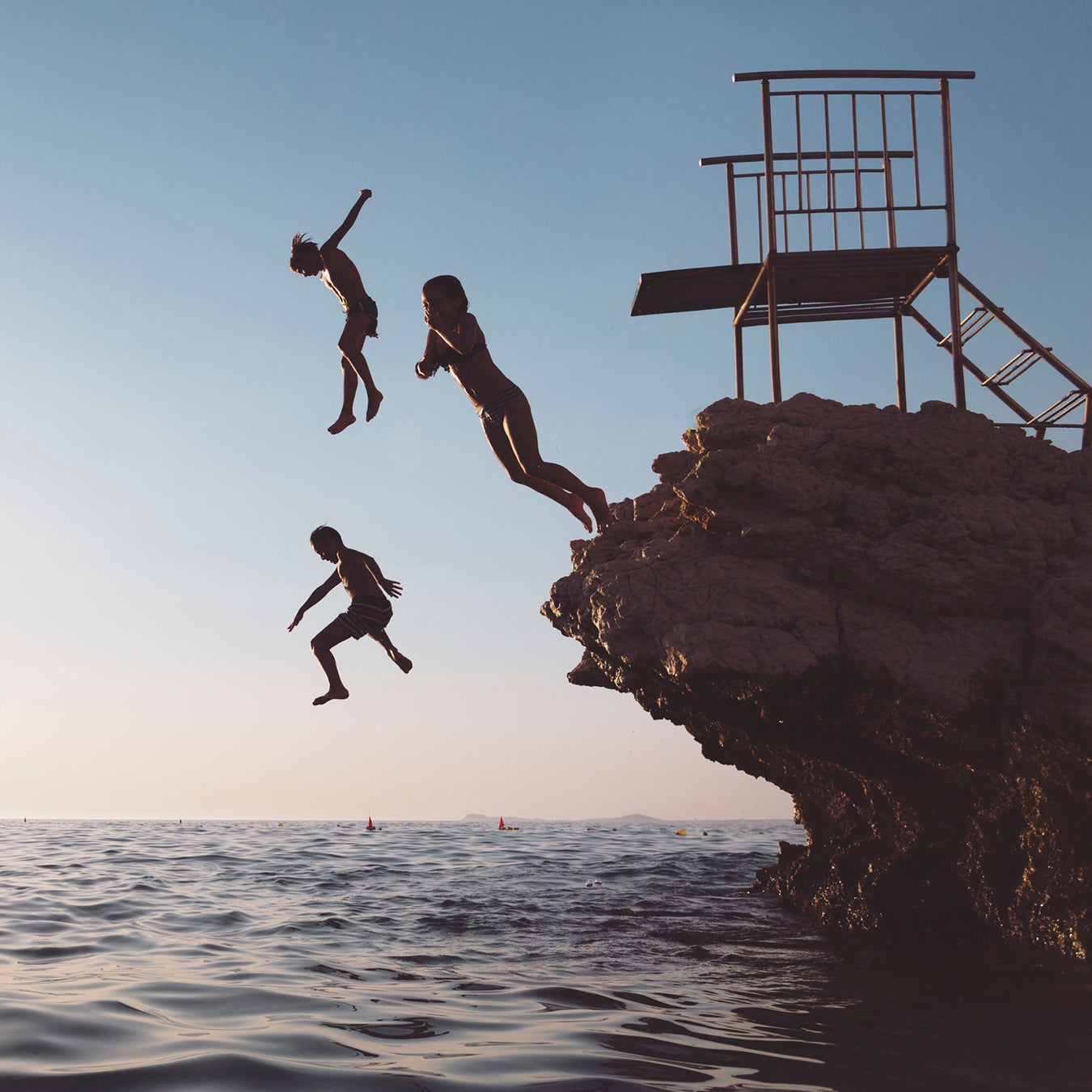 Silhouette of a group of children jumping from a cliff.