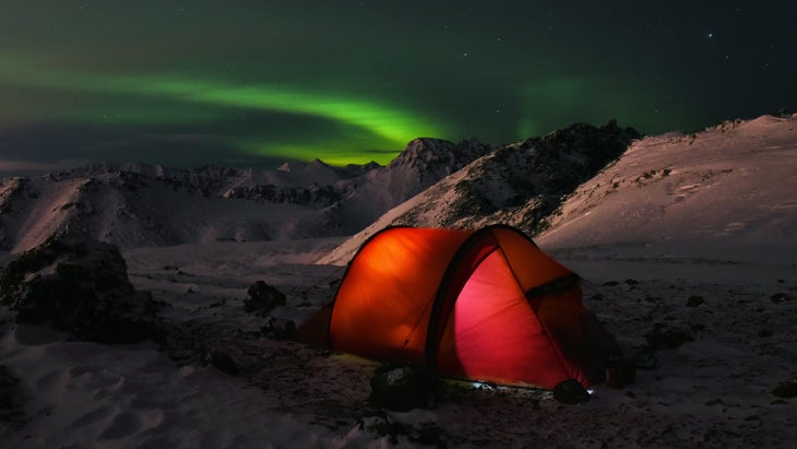 A red tent pitched on a mountain under the northern lights. To avoid altitude illness, gradually increase your sleeping elevation.