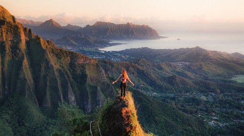 woman standing on ridge at sunset on oahu overlooking pacific ocean hawaii