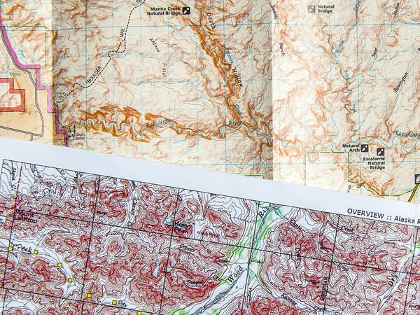 This close-up photo reveals how much topographic detail is compressed onto these maps. The map of Utah (rear) is at a scale of 1:75,000, or more than one mile per inch; the map of Alaska (front) is 1:250,000, or four miles per inch. These maps are most useful when planning a trip and may be sufficient in the field only for on-trail itineraries.