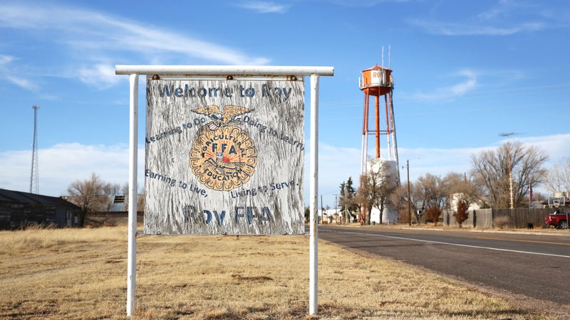 A sign welcoming you to Roy, with the iconic orange and white water tower looming in the background