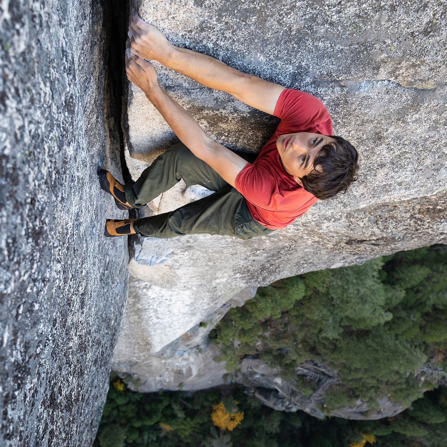 Climber in red t-shirt climbs a gray rock. A strong hand grabbed