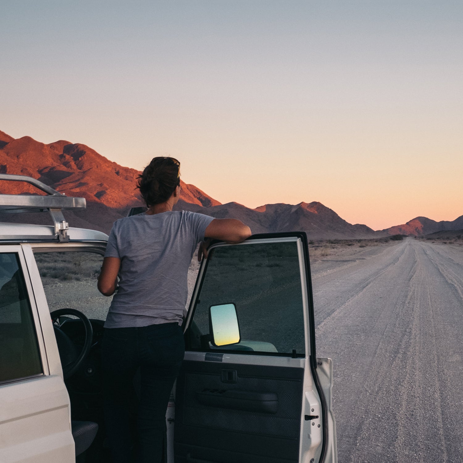 Woman On A Road Trip Through The Desert Leaning Out Of Her Car Watching A Sunset