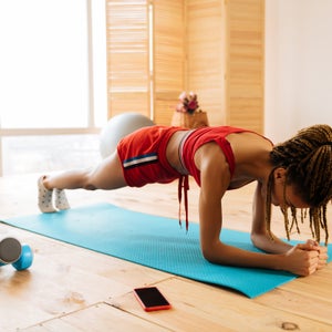 Woman with braids wearing red shorts standing in plank at home