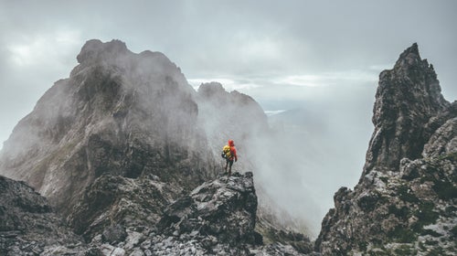 Male Mountaineer Standing On Top Of A Mountain In A Rugged Landsape