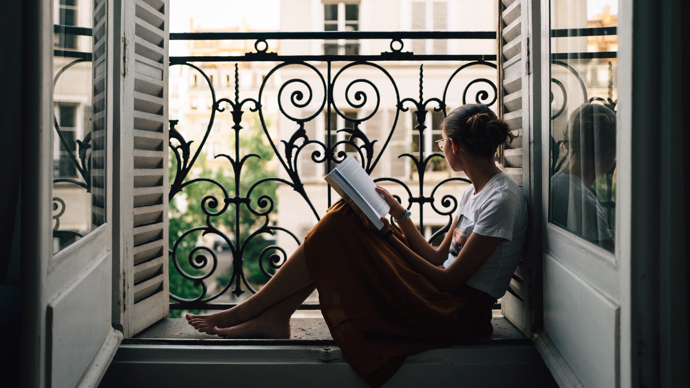 Girl Looking Out Of Apartment In Paris, While Reading Book.