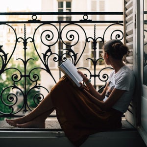 Girl Looking Out Of Apartment In Paris, While Reading Book.