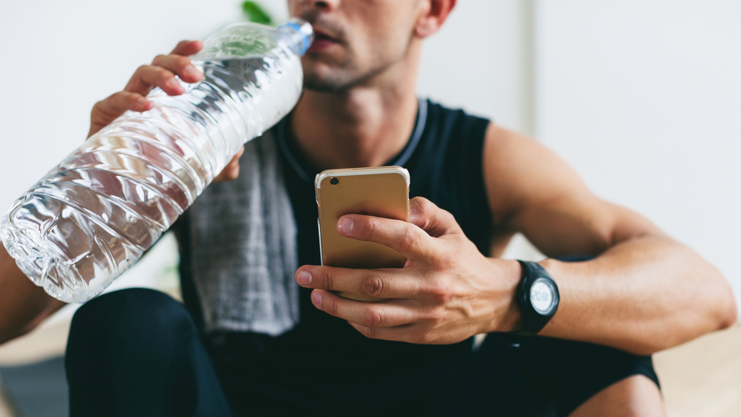 Closeup Of A Man Using His Phone Whilst Drinking Water After Hard Workout.
