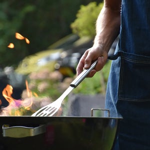Male arm holding a spatula over a grill