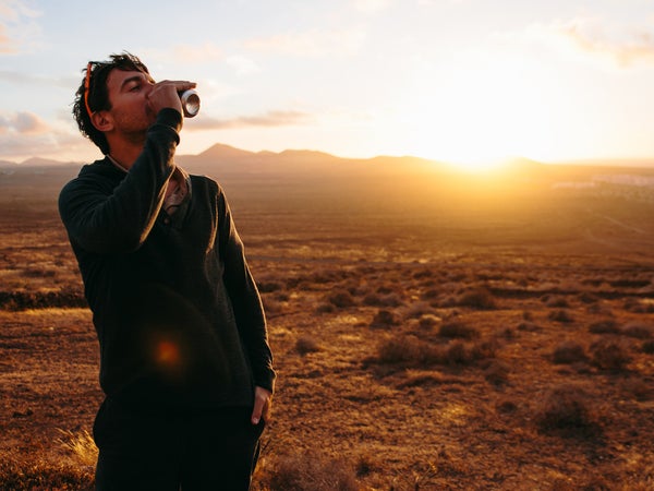 Adult Man Drinking From Can Against Of Sunset