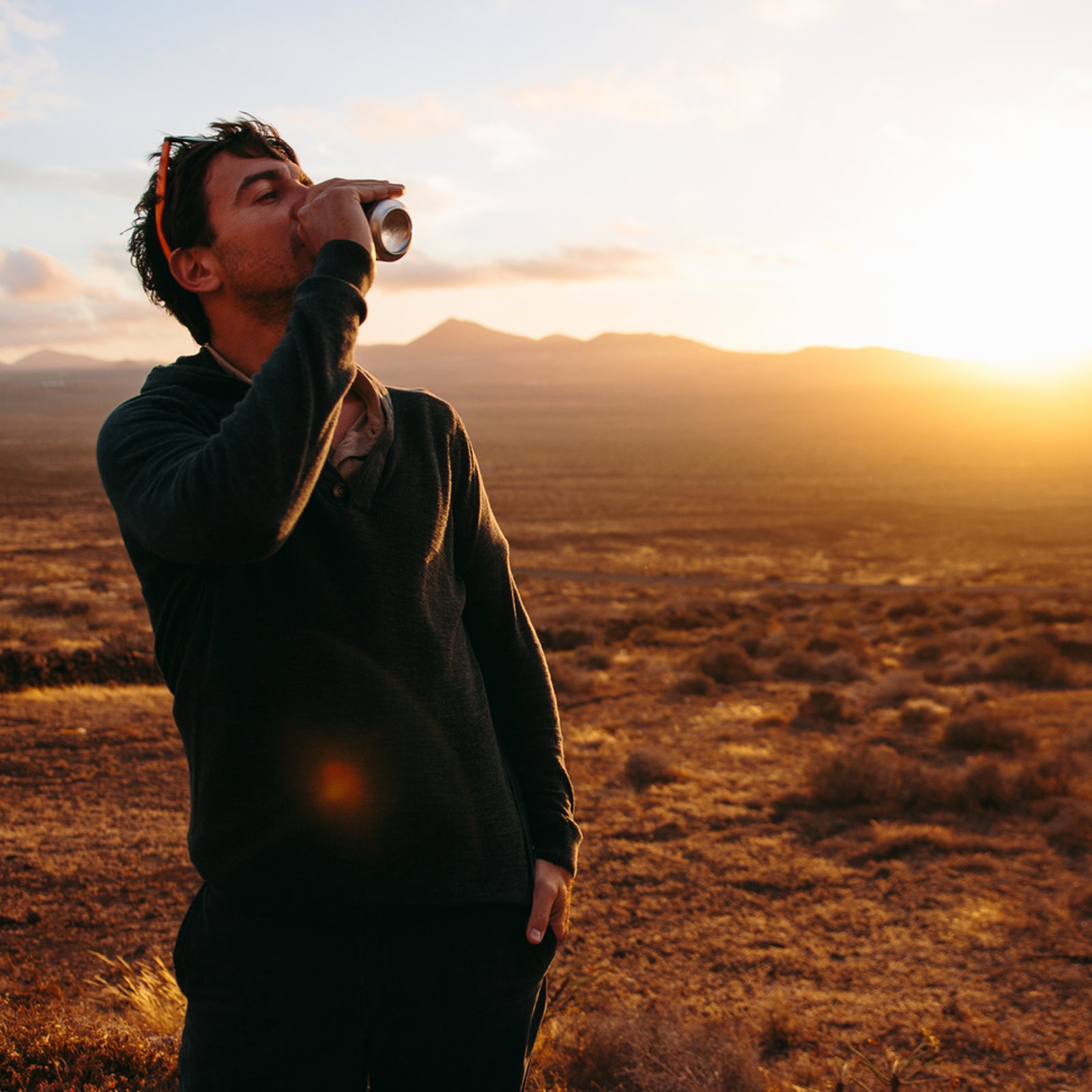 Adult Man Drinking From Can Against Of Sunset