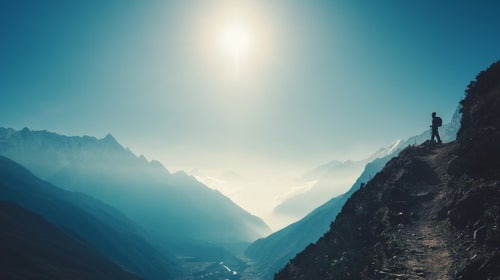 Standing woman on the hill against mountain valley at bright sunny day. Landscape with girl, trail, mountain, blue sky with sun and low clouds at sunset in Nepal.  Lifestyle, travel. Trekking