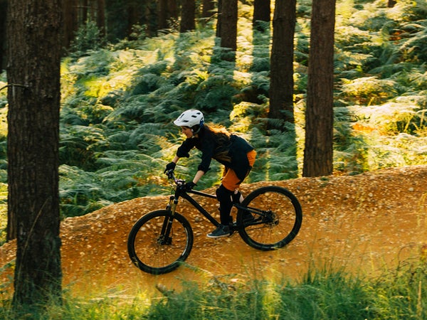 A Woman Cycling Down A Sandy Forest Path At Sunset