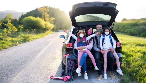 Family with two small daughters on trip outdoors in nature, wearing face masks.