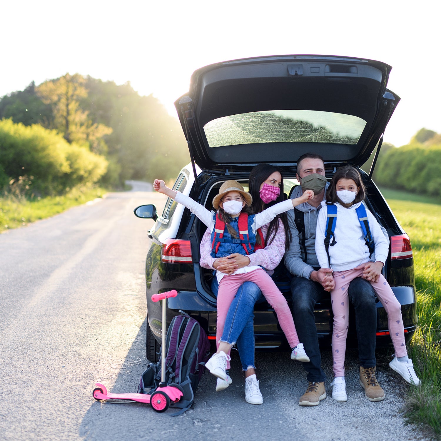 Family with two small daughters on trip outdoors in nature, wearing face masks.