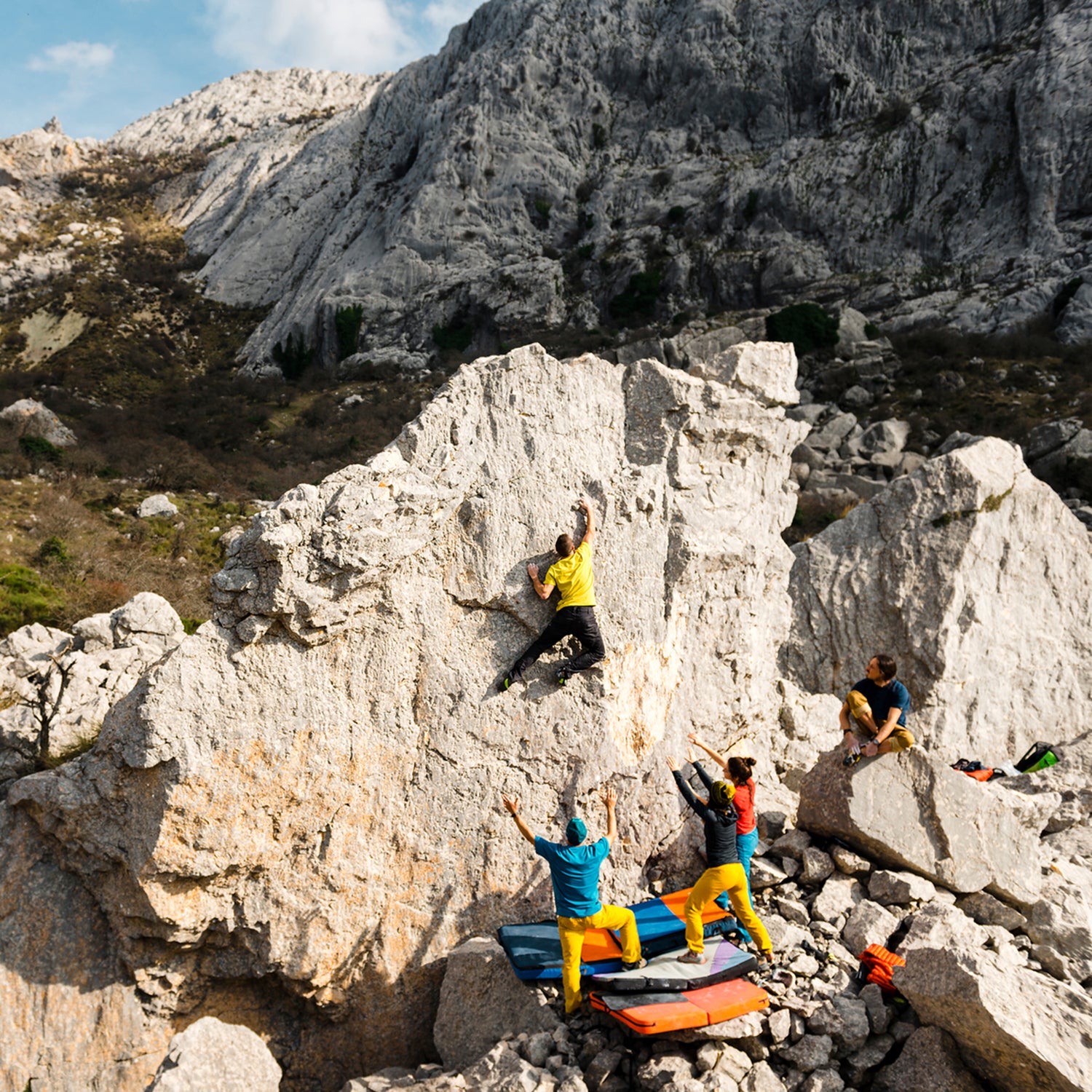 Young Man Climbing To The Top Of Large Boulder Spotted By Friends