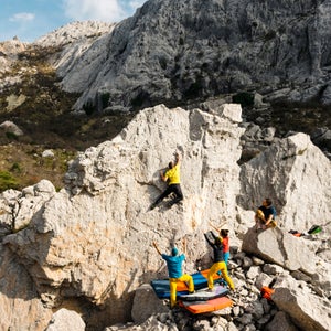 Young Man Climbing To The Top Of Large Boulder Spotted By Friends