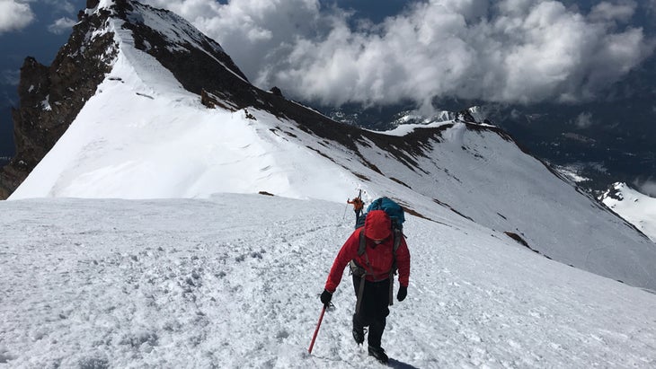 A climber in a red jacket ascends a snowy ridge