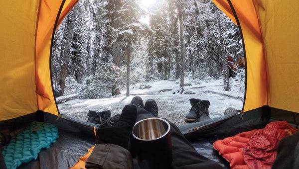 Camping with hand holding cup in yellow tent with snow in pine forest
