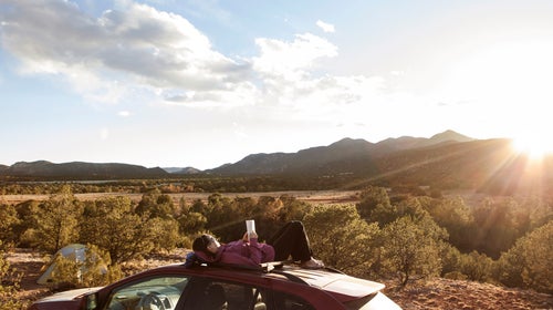 Girl Laying On Top of Car Reading