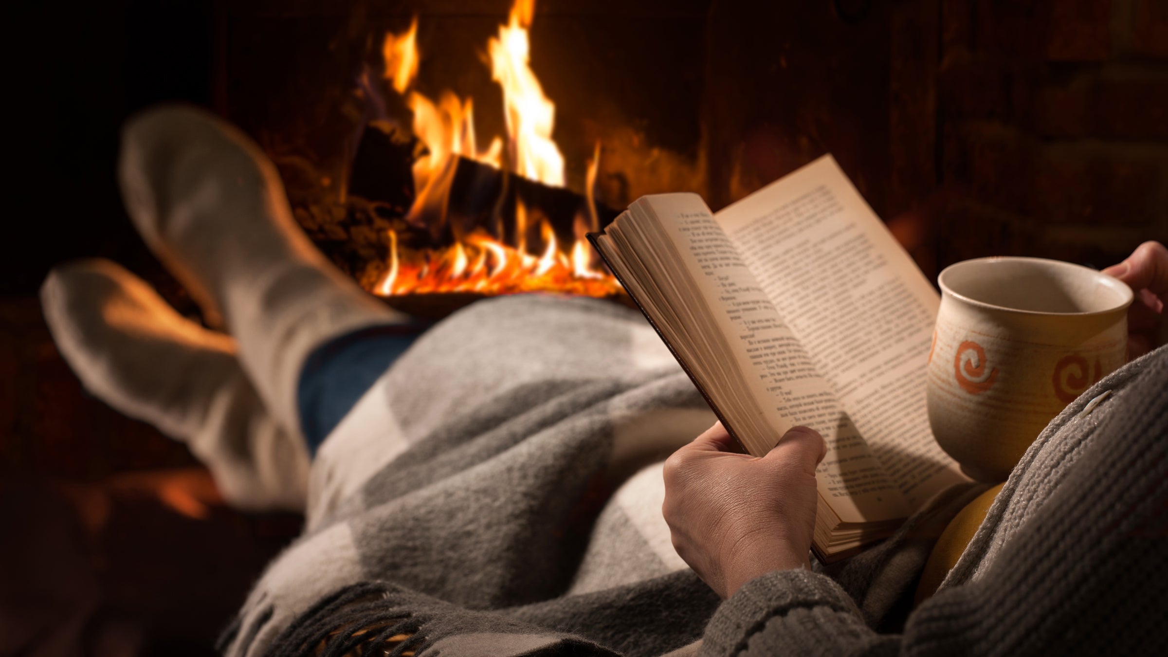 Woman reads book near fireplace