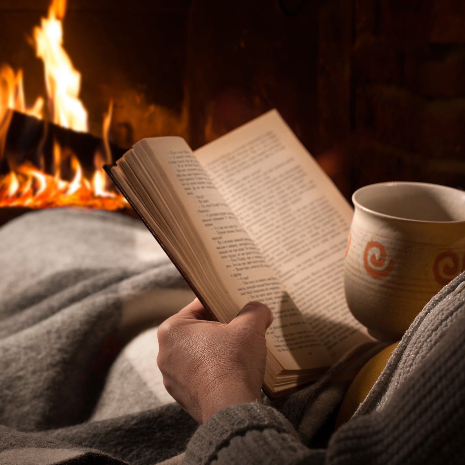 Woman reads book near fireplace