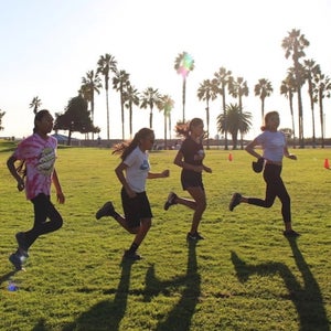 Wings of America youth runners doing strides against sunny landscape with palm trees.