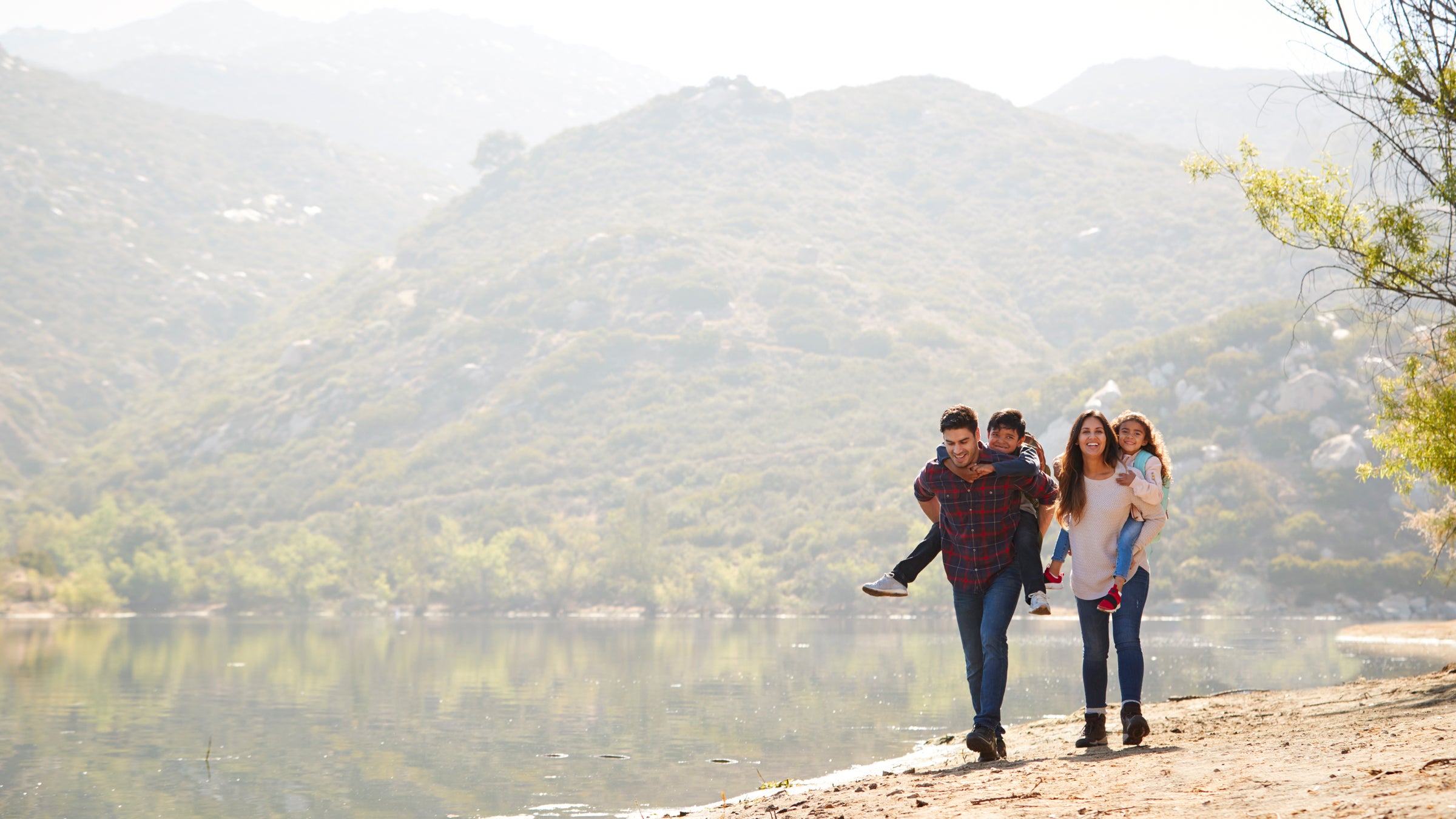 Parents piggybacking their young children by a mountain lake