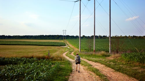 A hiker crosses on the Appalachian Trail through corn fields in pennsylvania.