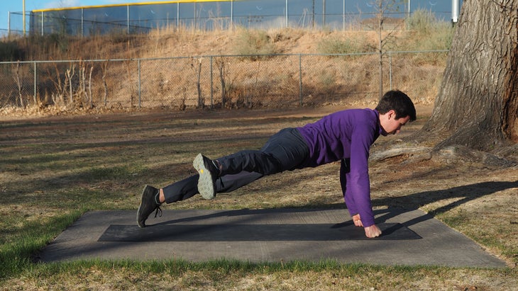 man in high plank on fists kicking right leg out to right side