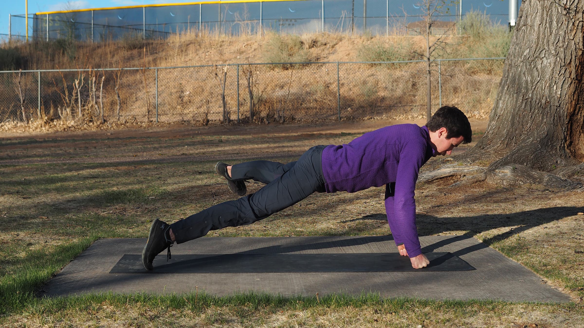 man in high plank on fists kicking left leg out to left side