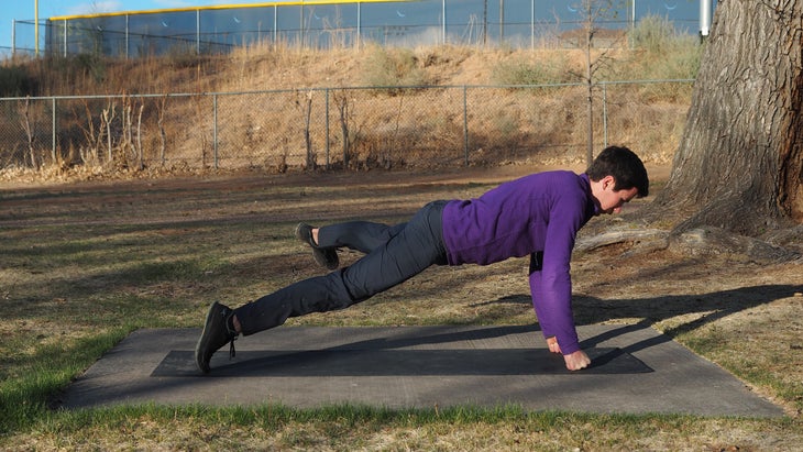 man in high plank on fists kicking left leg out to left side