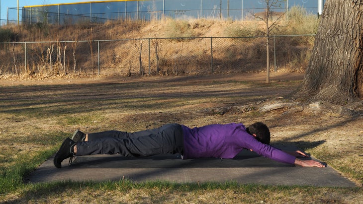 man with belly on ground with arms outstretched overhead