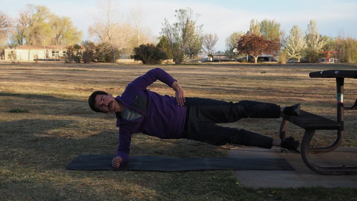 a man with one arm on hip and the other on ground raising up with one leg high on a bench and one low hovering over ground