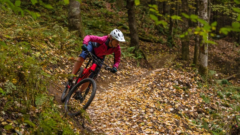 Woman mountain biker corners through autumn leaves