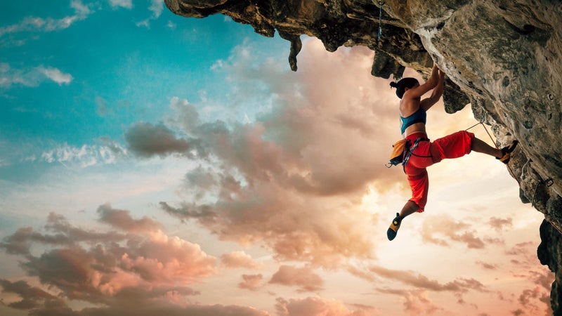 Athletic Woman climbing on overhanging cliff rock with sunset sky background