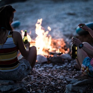 A group of young people gathered on a beach around a campfire..