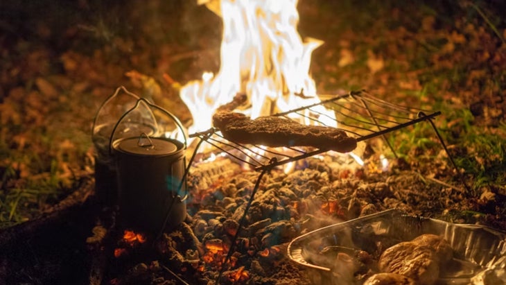 Steak cooks on a grill grate over a campfire