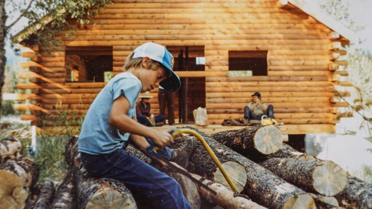 Young Aaron prepares logs for the next campfire while his grandfather’s cabin is under construction.